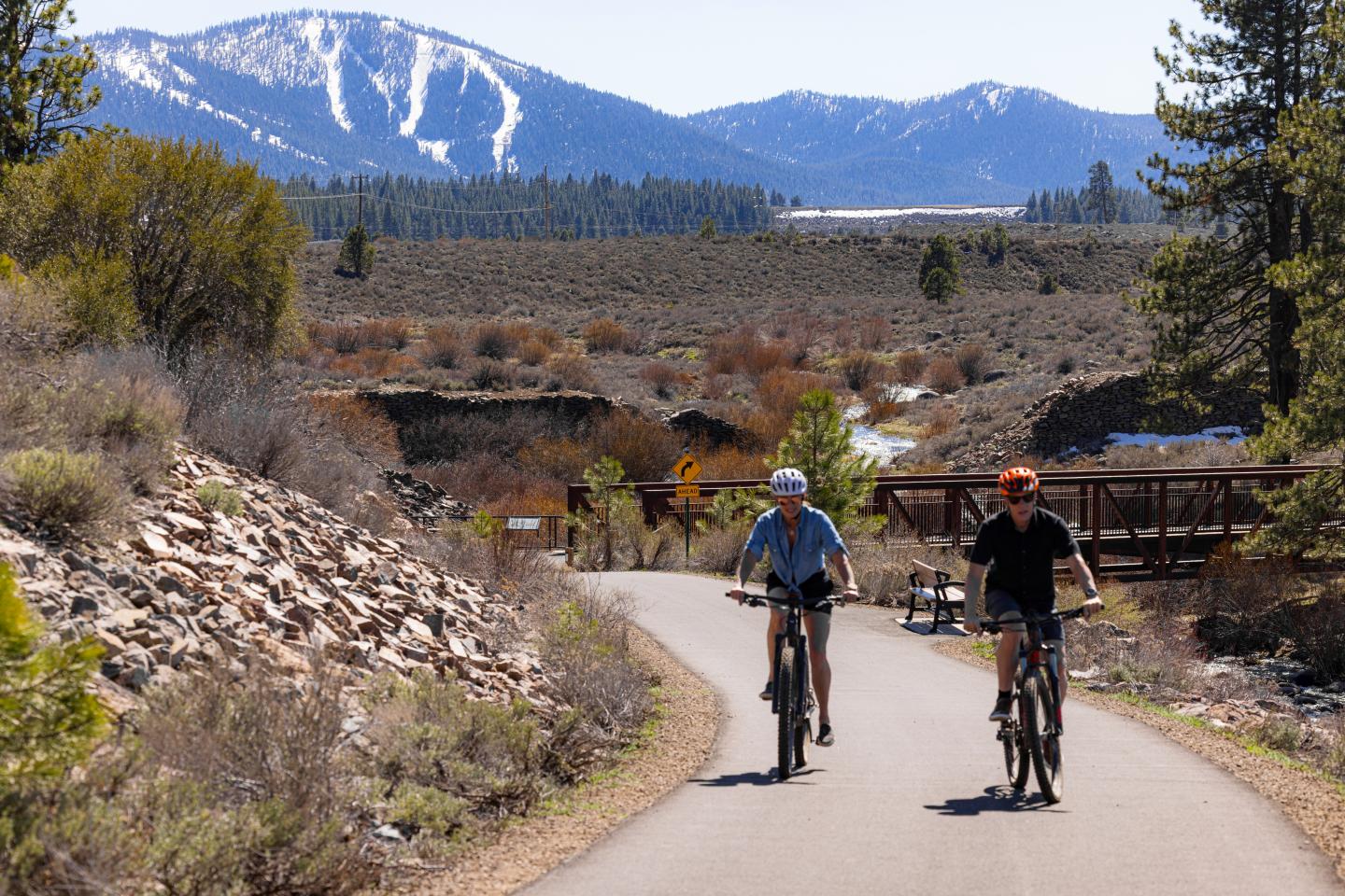 Two people biking on a path with mountains in the background.