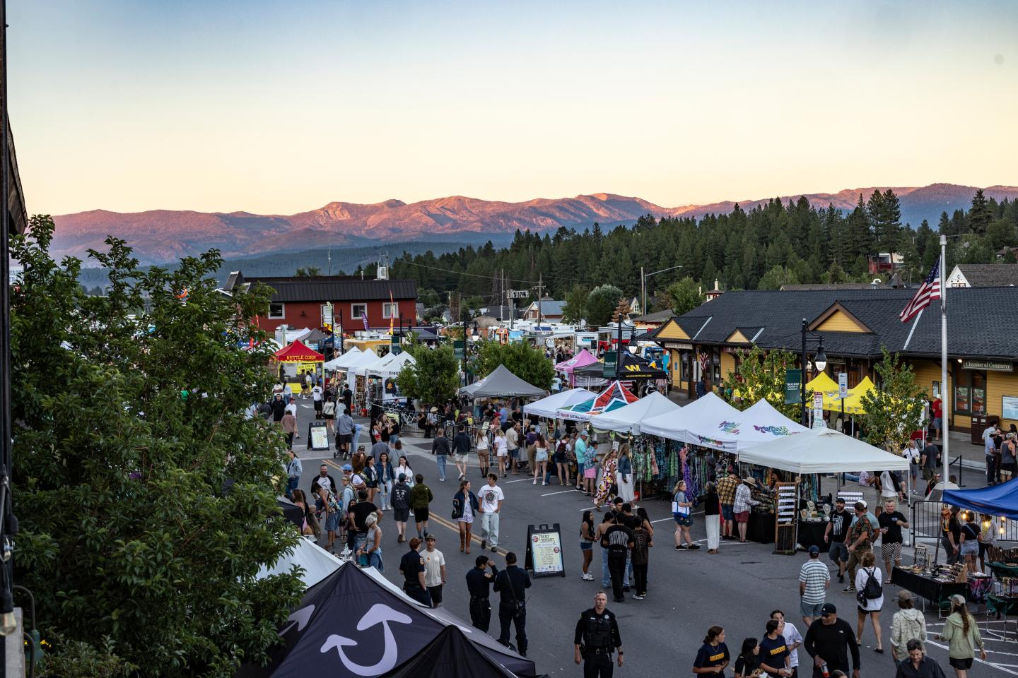 Street fair with tents and people, set against a mountain sunset backdrop.