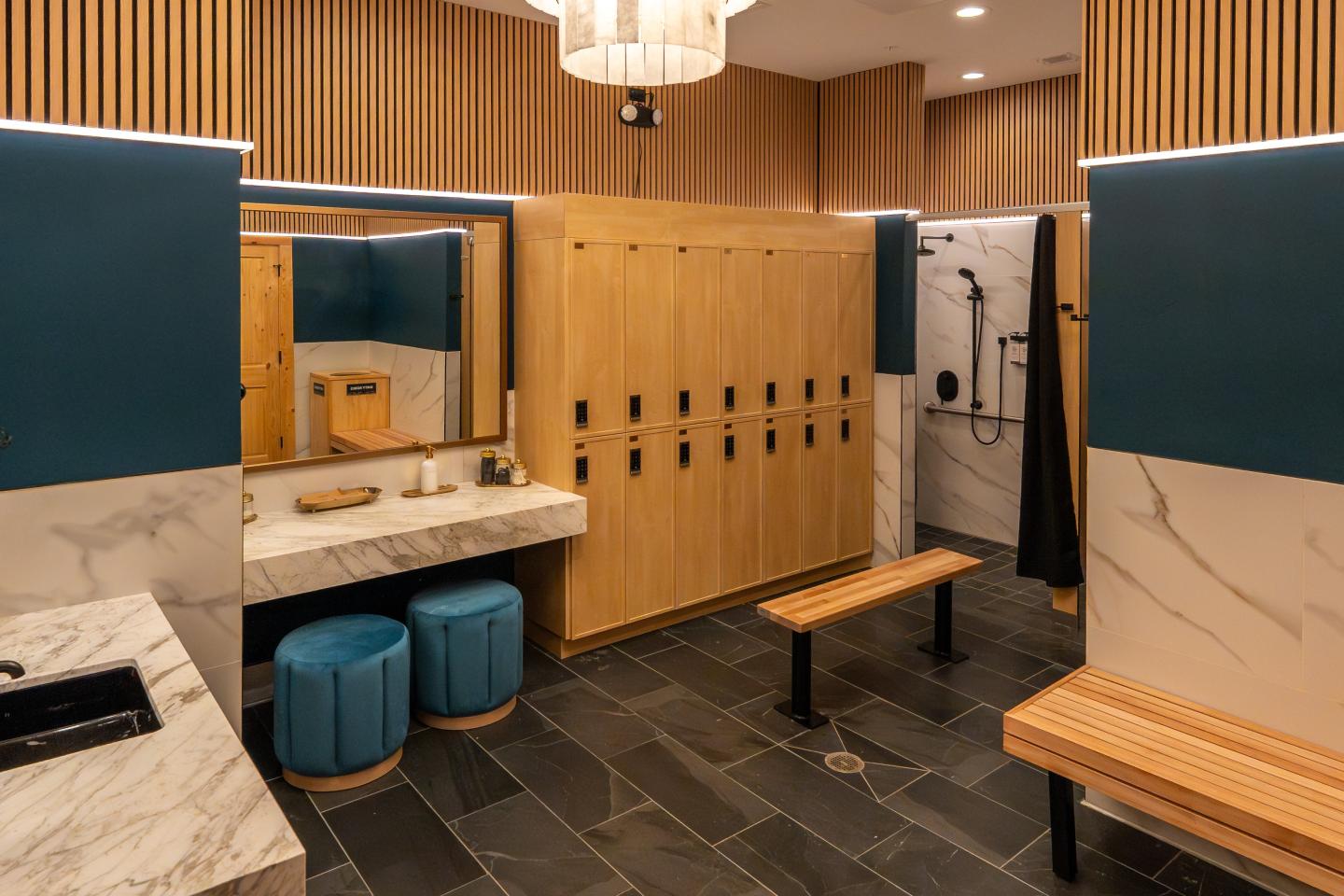 Modern locker room with wooden lockers, benches, and a marble sink area.