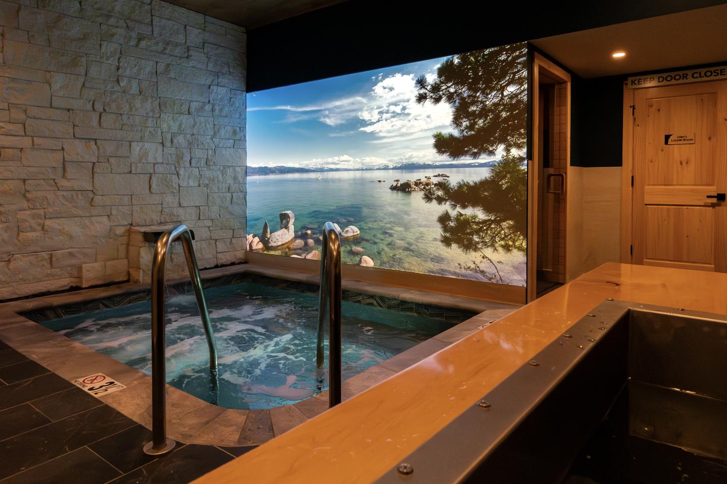 Indoor pool with a scenic ocean view through a large window, wooden accents around.