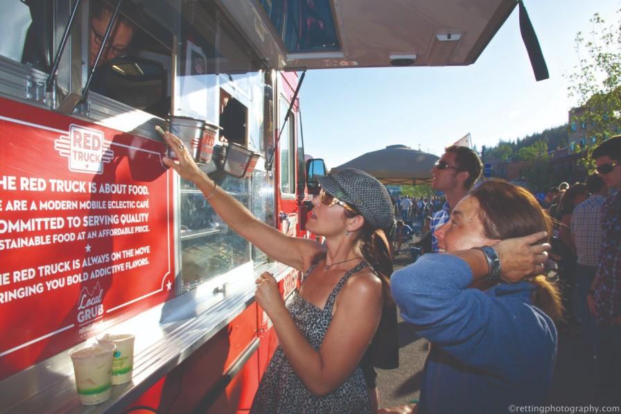 People ordering food at a red food truck on a sunny day.
