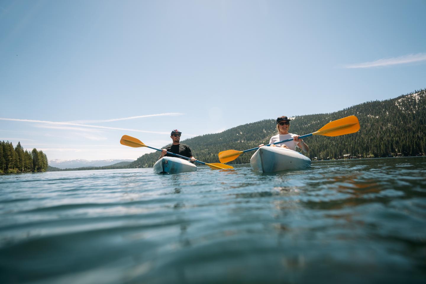 Two people kayaking on a serene lake under a clear blue sky.