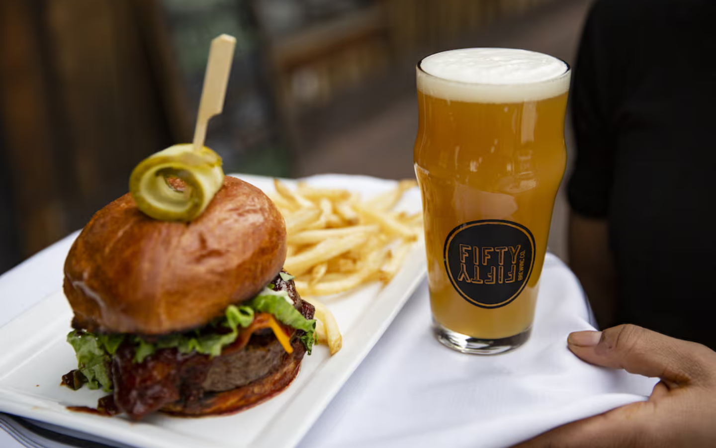 Burger with fries and a pint of beer on a table.