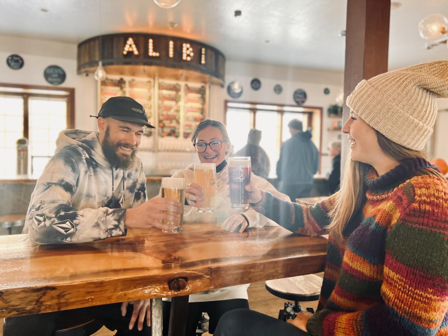 Three friends toasting with drinks at a cozy pub table.