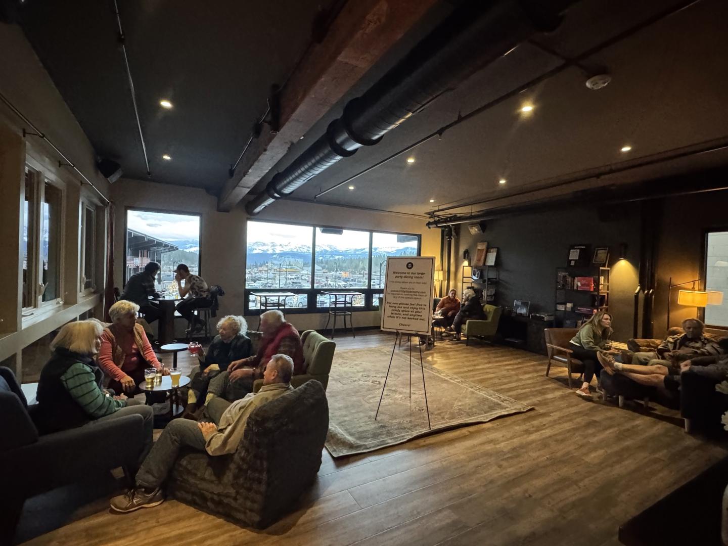 Cozy lounge with people seated, large window view of mountains.