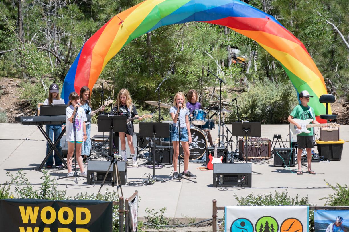 Colorful band performing outdoors under a rainbow canopy.