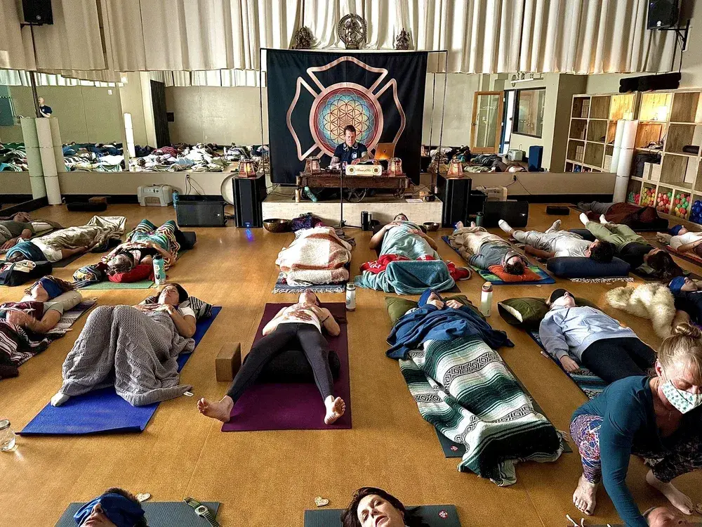 People lying on mats in a yoga studio, meditating with a musician on stage.