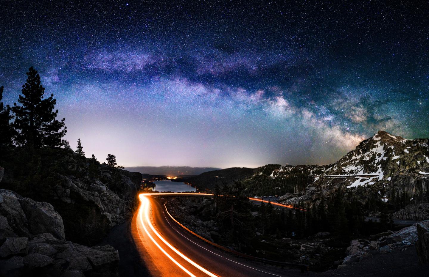 Curving road at night with car light trails under a starry sky.