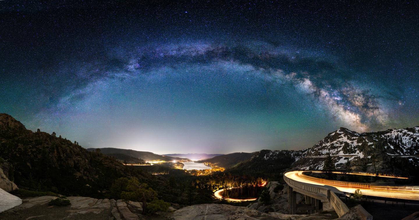 Starry night sky over a mountain landscape with city lights below.