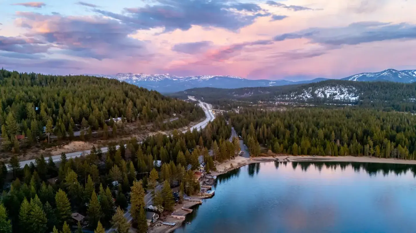 Scenic lake and forest at sunset with a winding road in the distance.
