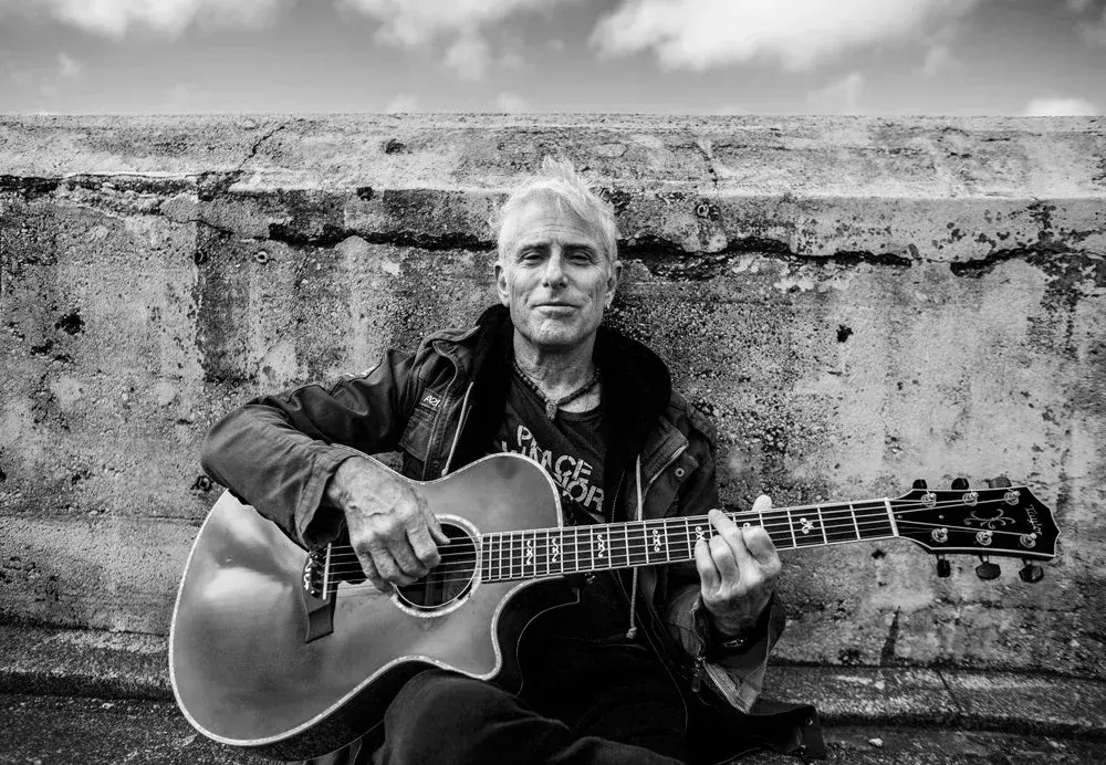 Man playing guitar against a concrete wall, black and white photo.