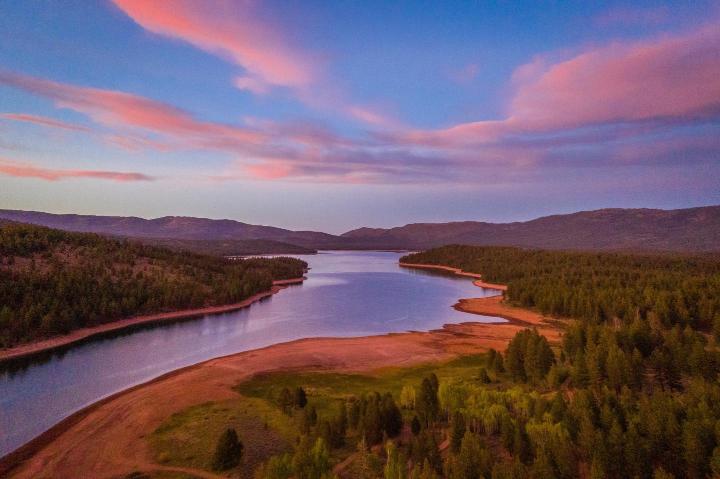 Colorful sunset over a winding river and forest, with pink clouds and vibrant greenery.