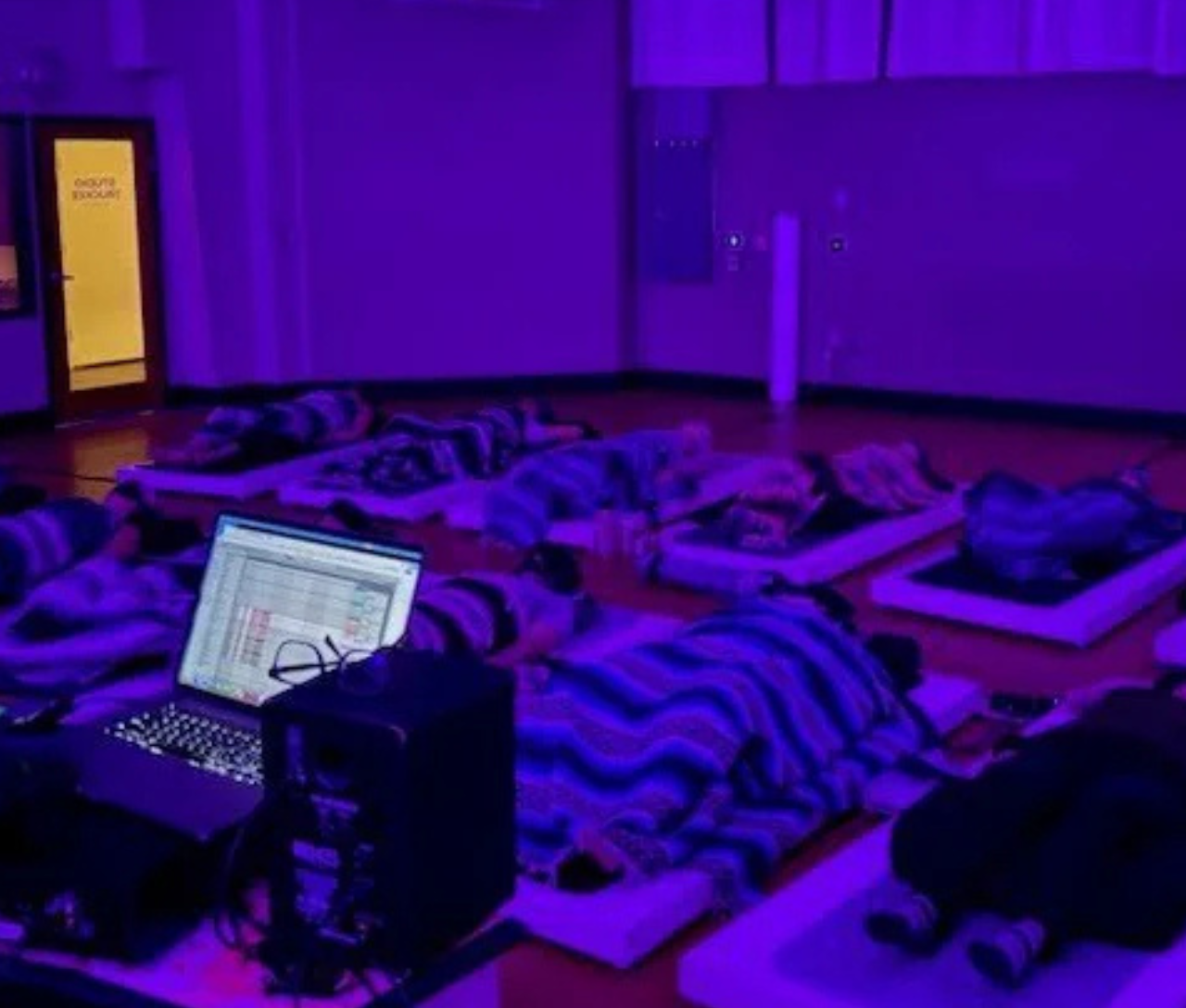 People lying on mats under purple light, with a laptop nearby.