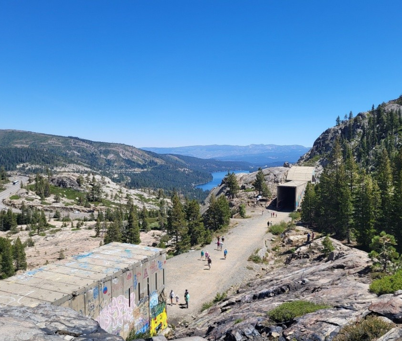 Mountain path with people, lake view, clear blue sky.