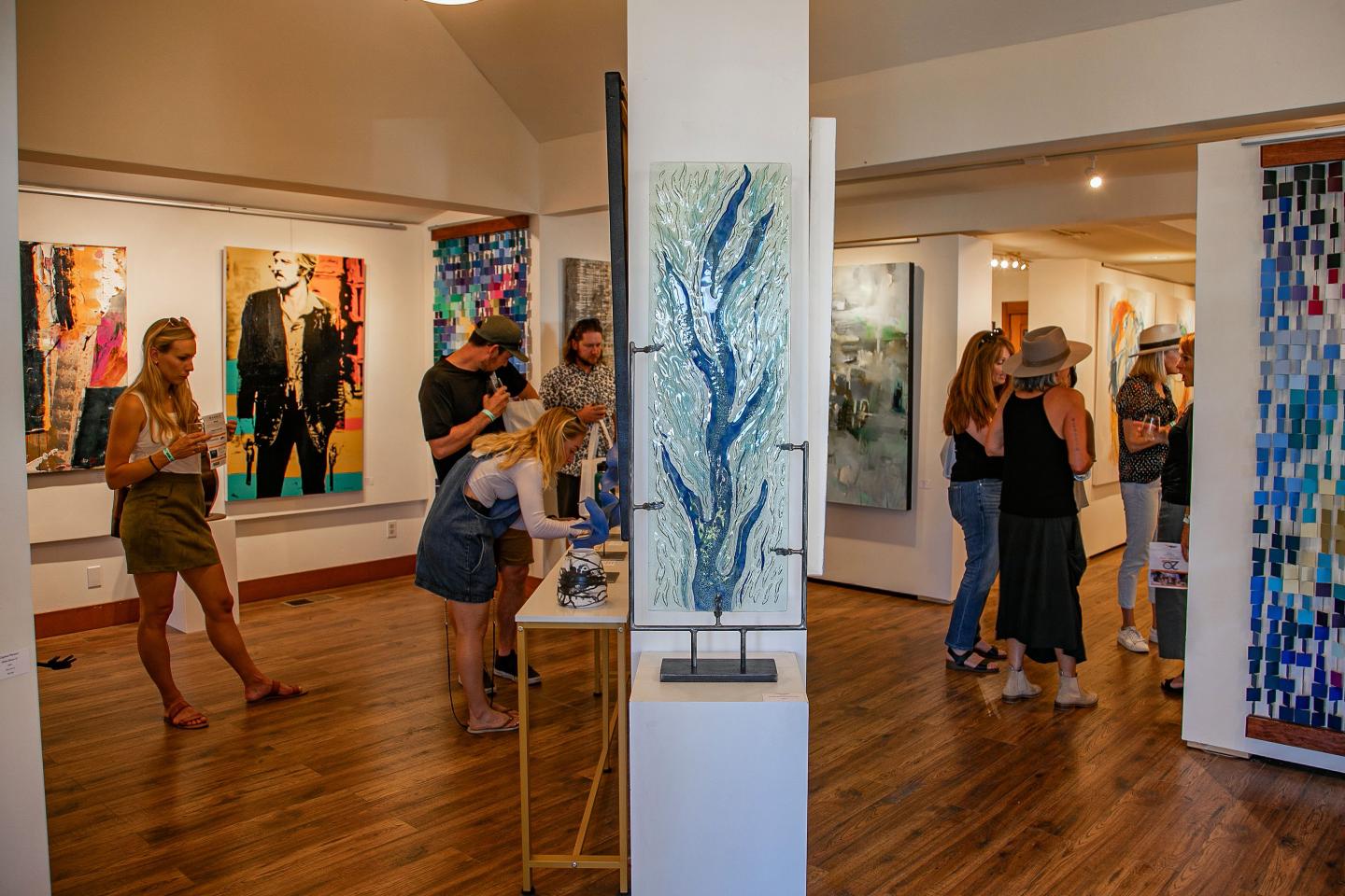 Art gallery with people viewing colorful paintings and sculptures on display.