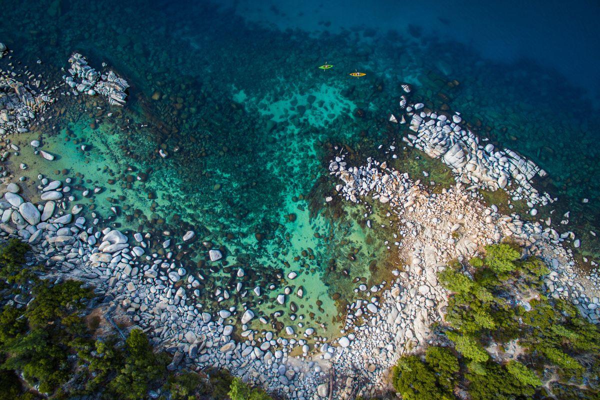 Rocky shoreline with turquoise water and green foliage.