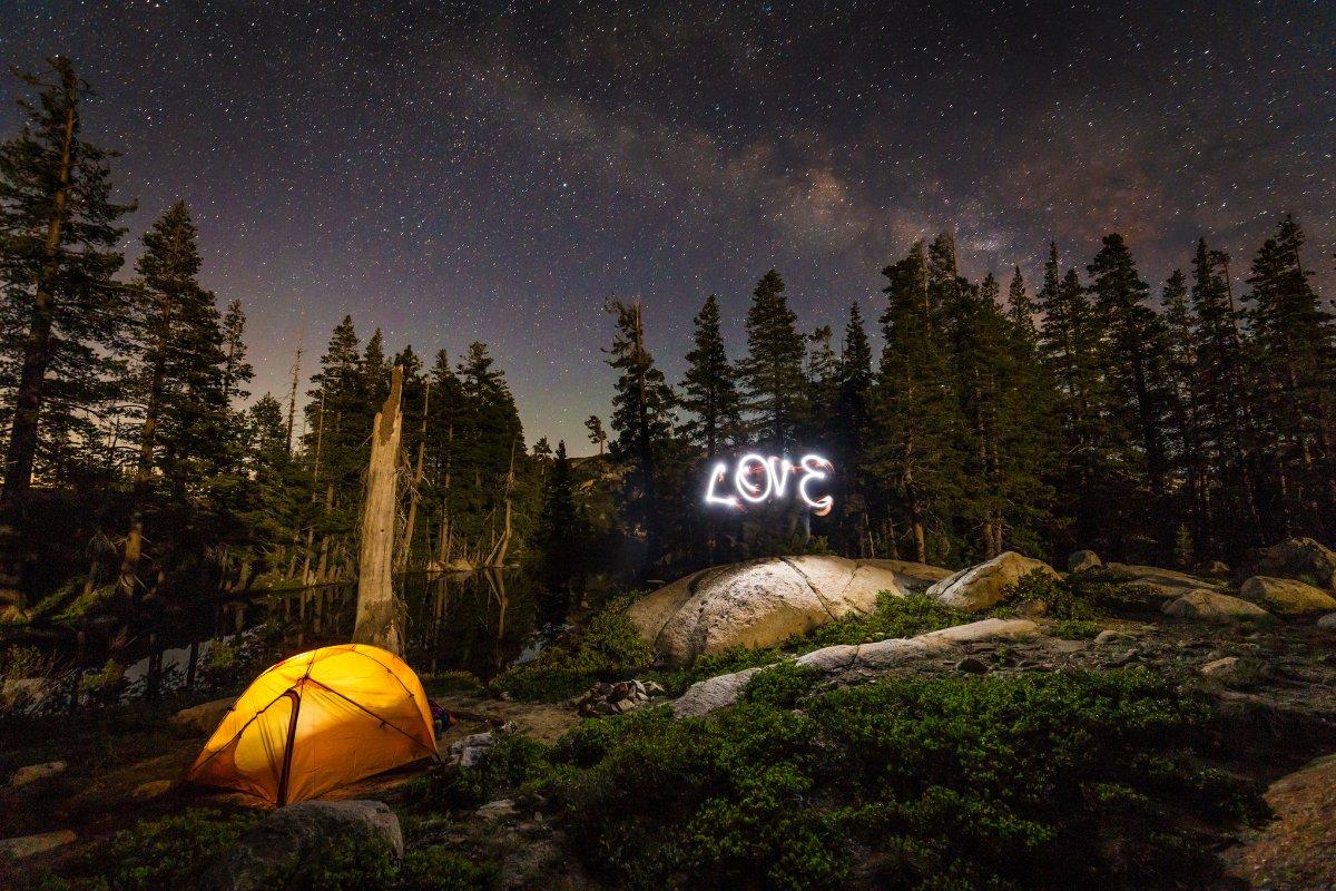 Tent under starry sky with "Love" written in light against a forest background.