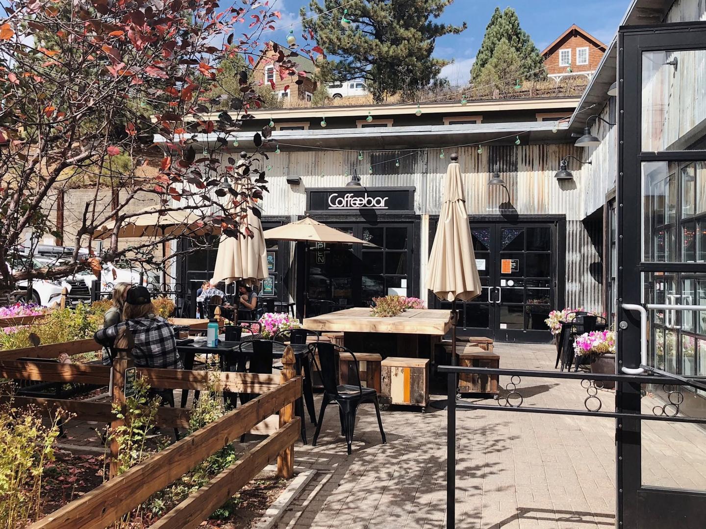 Outdoor café with tables, umbrellas, and patrons in a sunny setting.