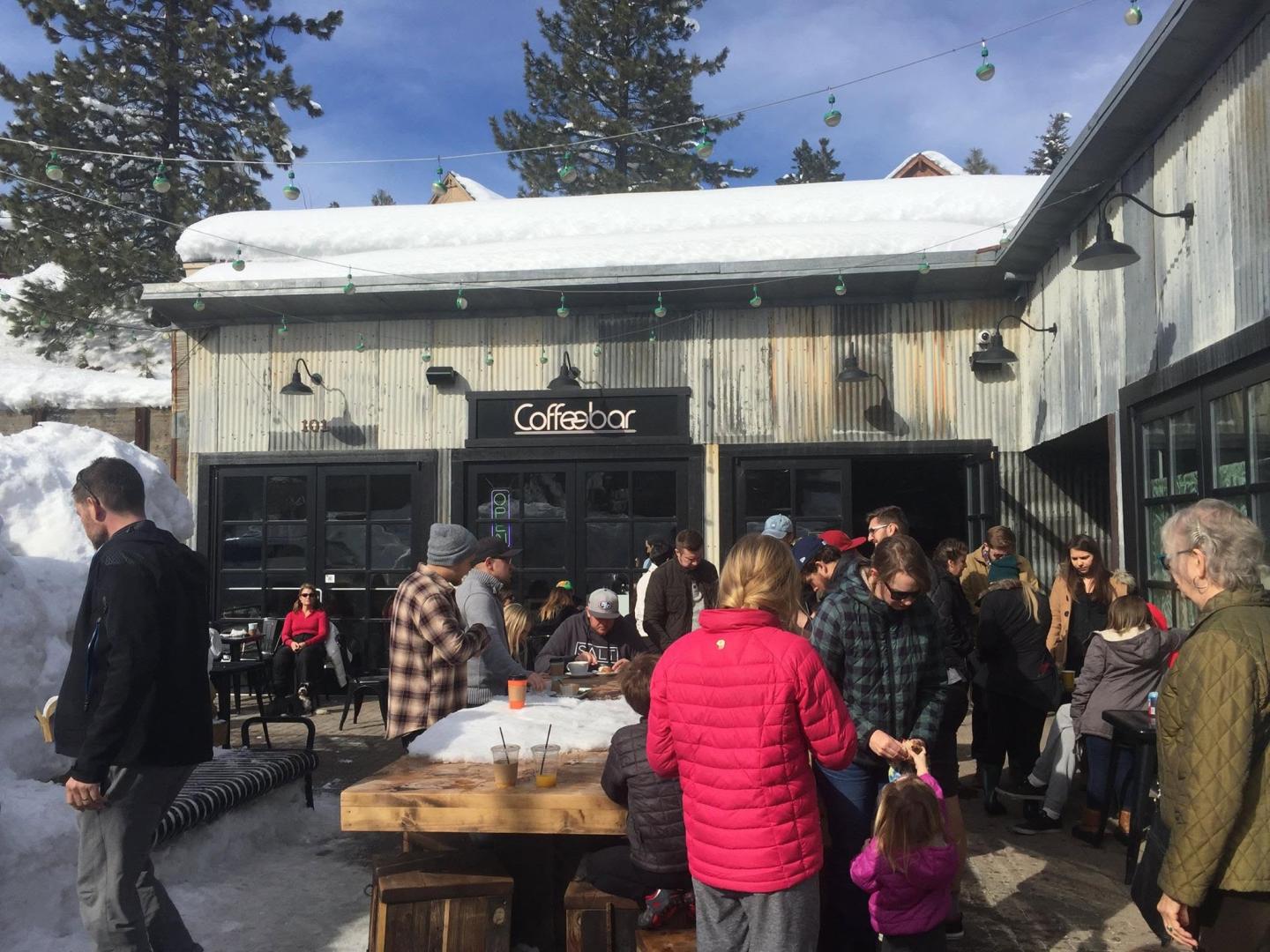 Crowd gathers outside a snowy café on a sunny day.
