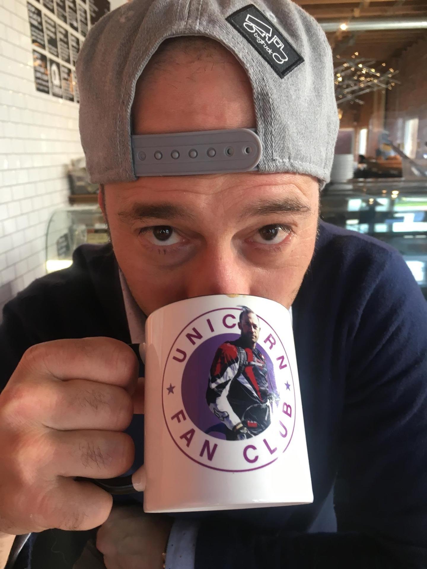 Man with backwards cap sipping from a "Unicorn Fan Club" mug.