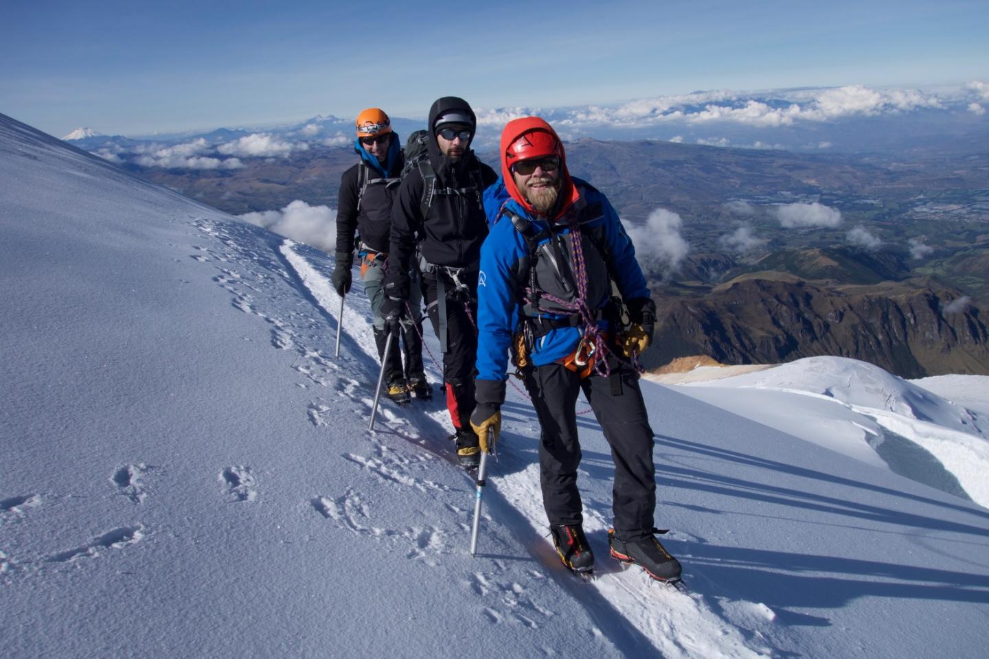 Climbers ascending snowy mountain ridge under clear sky.