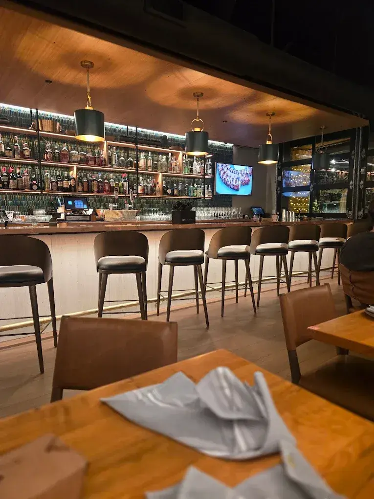 Bar with stools, warm lighting, and a wooden table in the foreground.