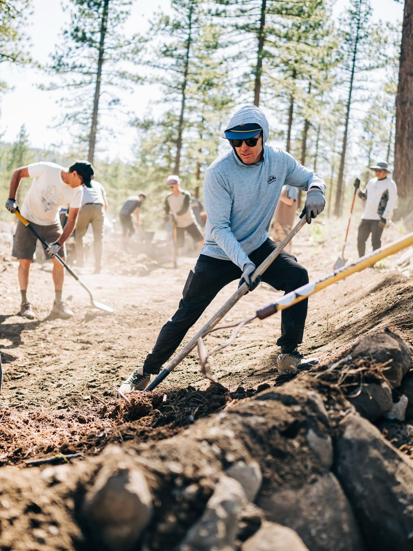 People working on a dusty trail with shovels in a forest setting.