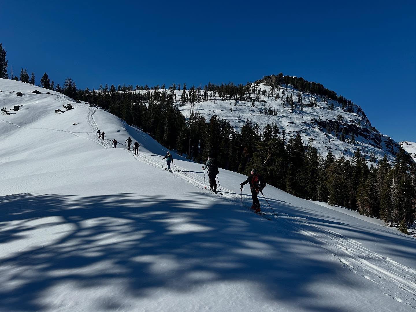 Skiers ascending a snowy mountain under a clear blue sky.