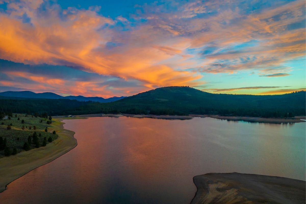 Calm lake at sunset with vibrant orange and blue sky, surrounded by hills.