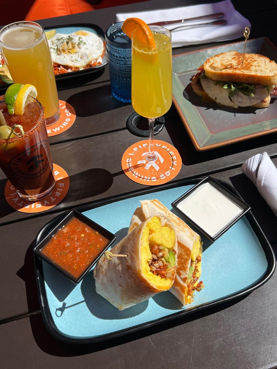 Brunch spread with drinks, sandwiches, and dipping sauces on a table.