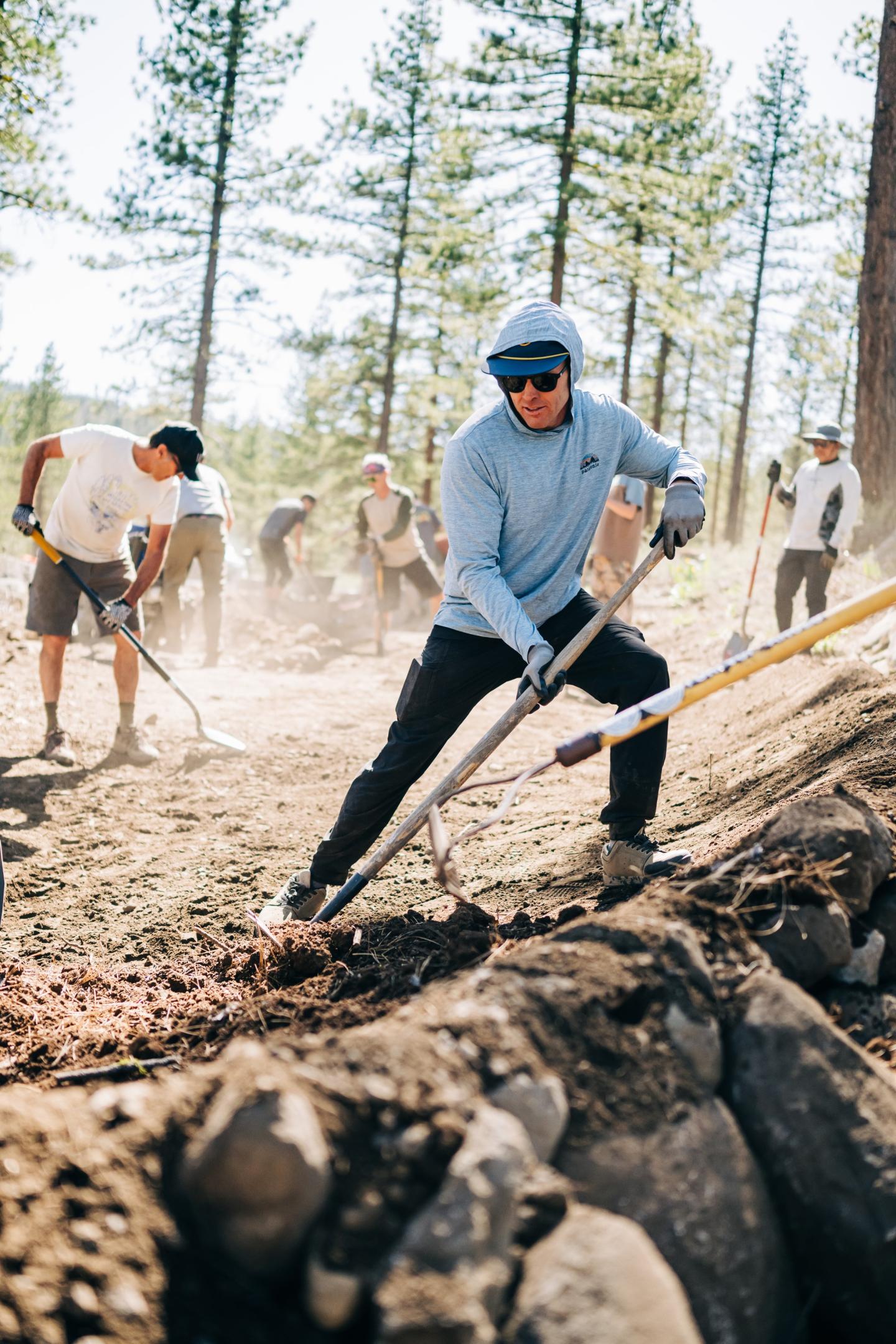 People digging a trail in a forest, wearing casual outdoor clothing.