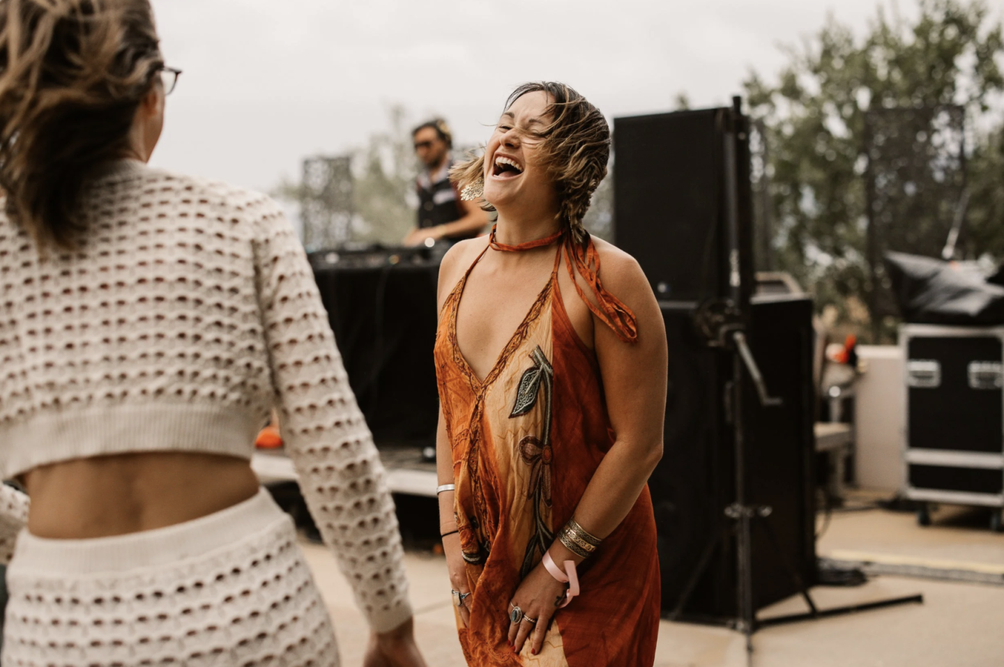 Woman in orange dress dancing and laughing outdoors at an event.