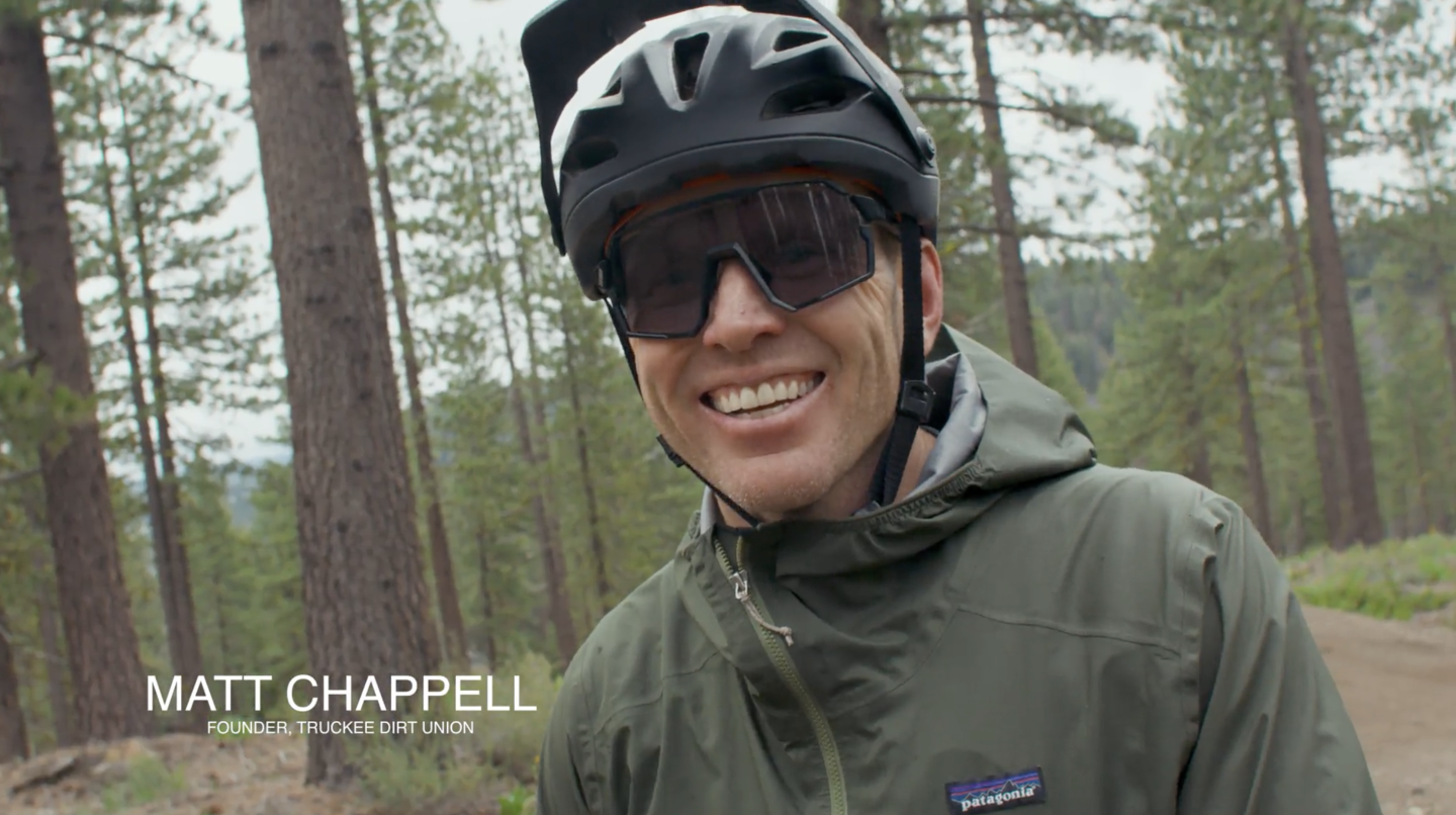 Smiling cyclist in helmet and sunglasses on forest trail.