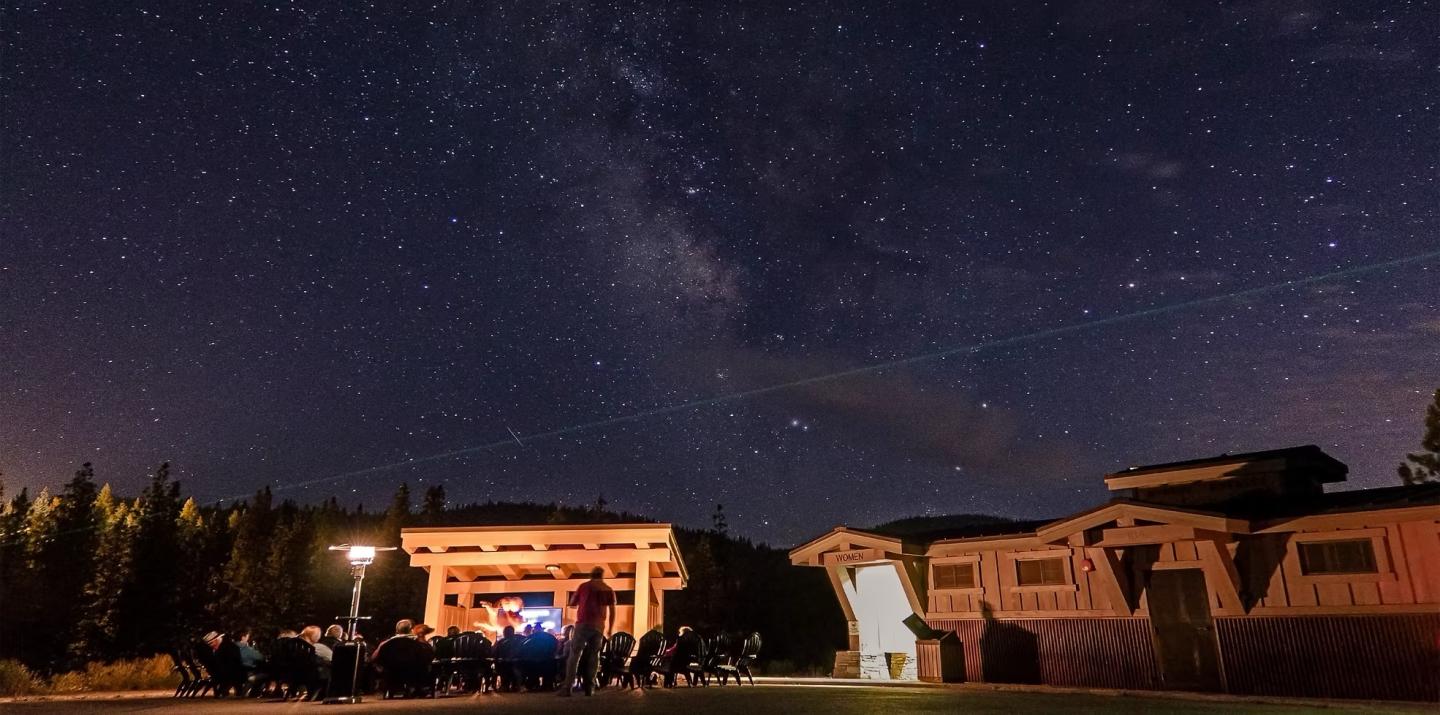 Starry night sky with a building and silhouettes of people gathered outside.