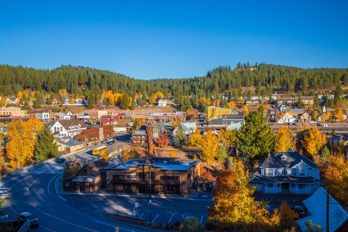 Colorful town in autumn, surrounded by trees and hills under a clear blue sky.