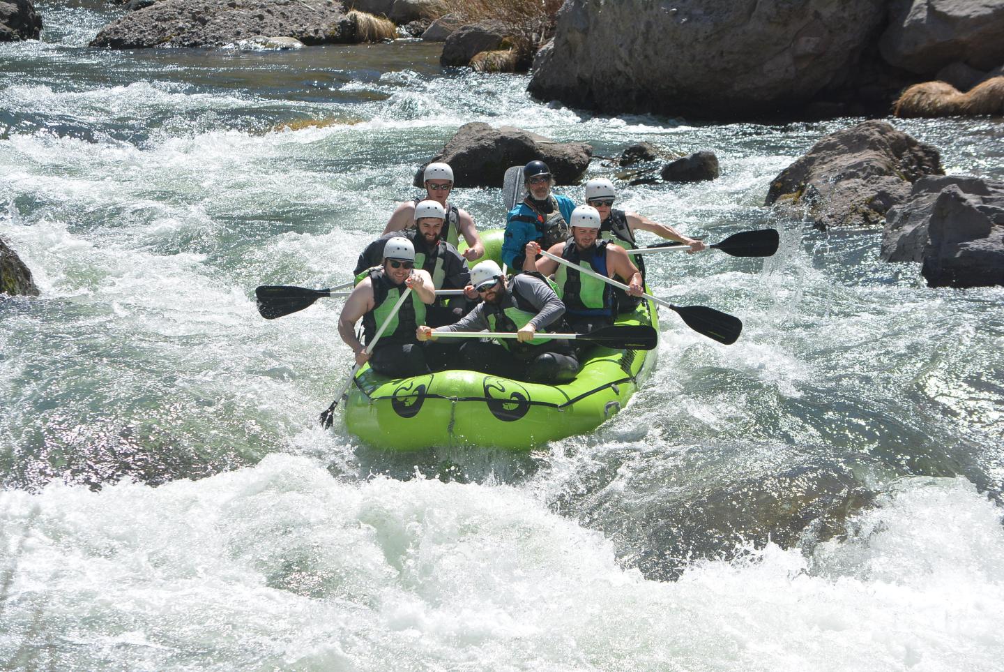 Group rafting on a rapid river in a green inflatable raft.