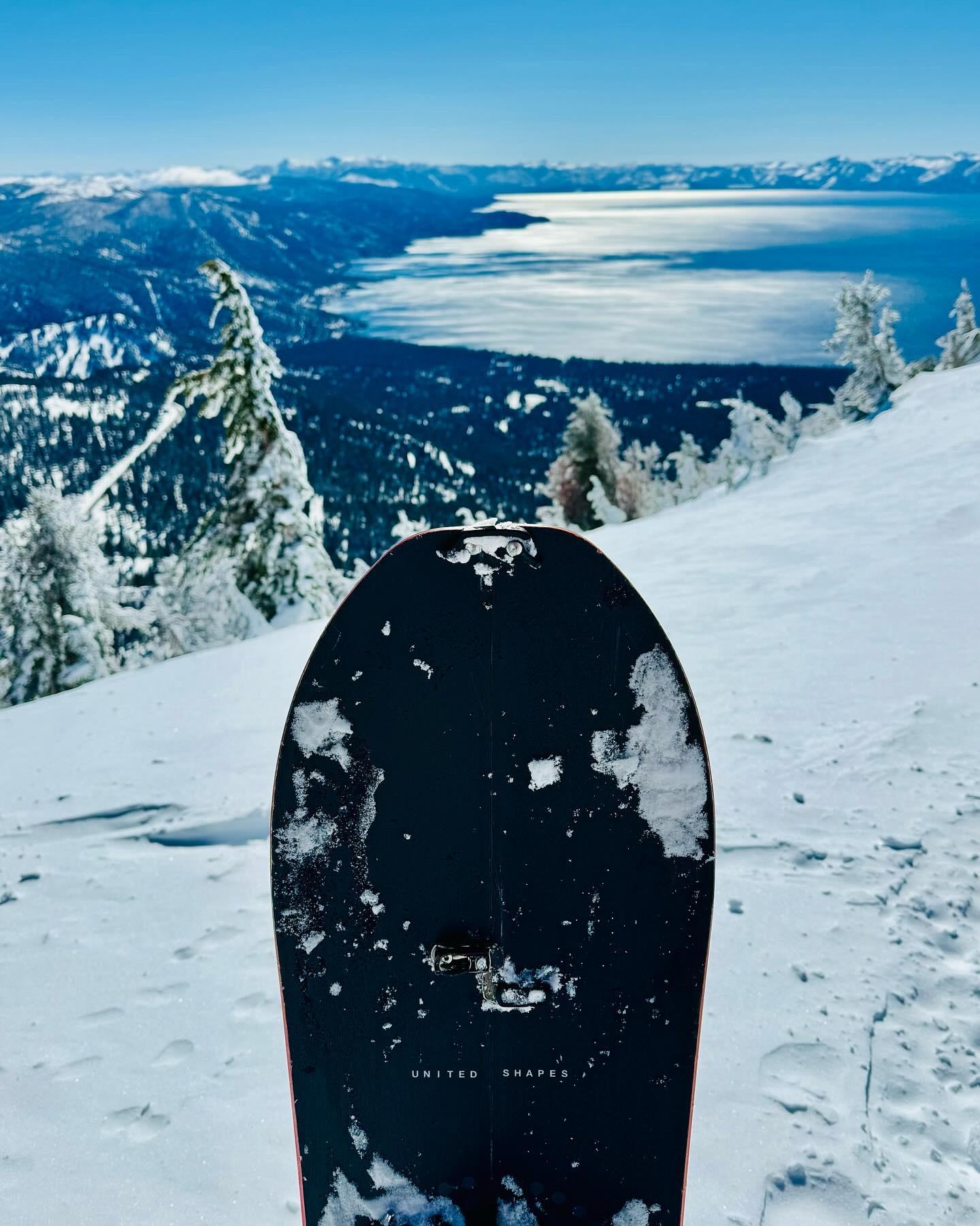 Snowboard on snowy slope overlooking a lake and mountains.