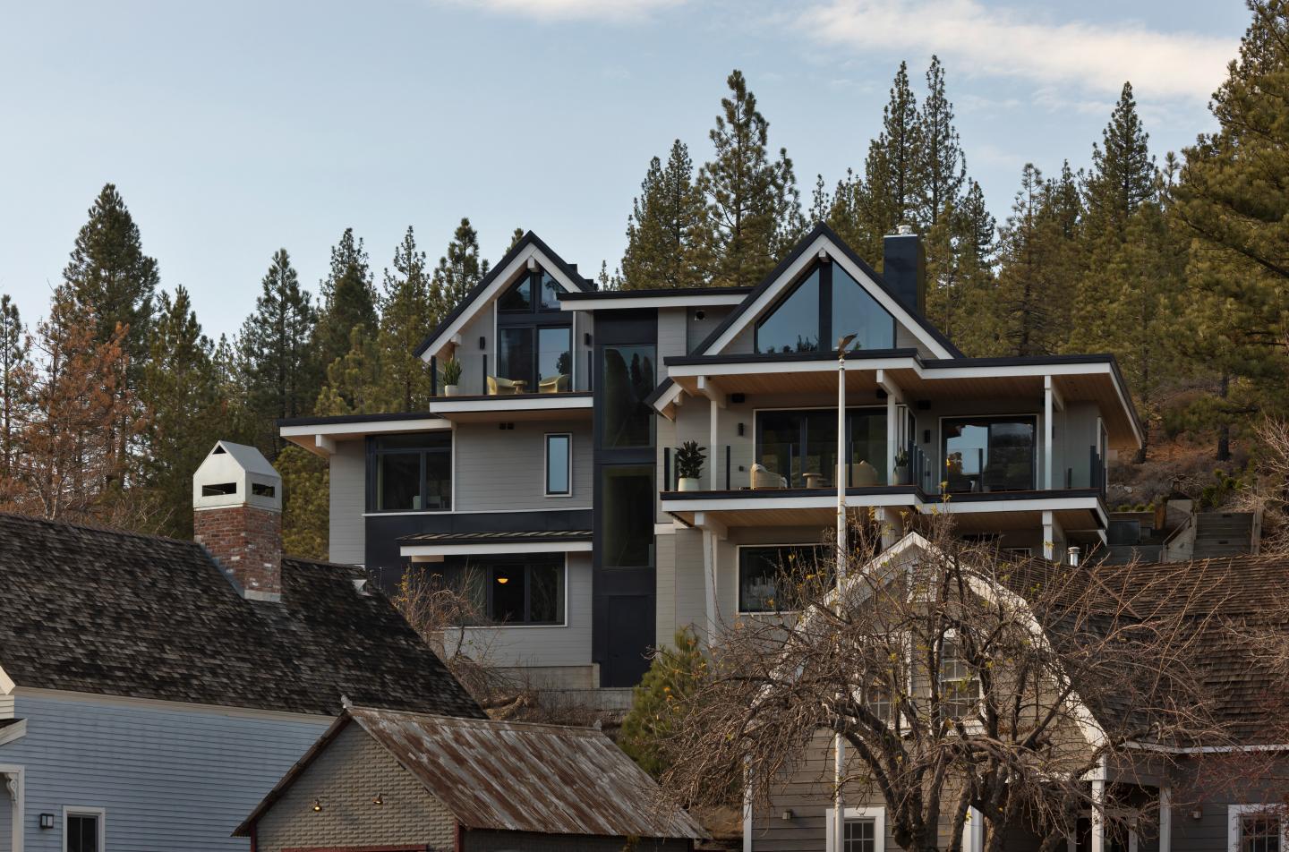 Modern house with angular roofs surrounded by trees and smaller buildings.