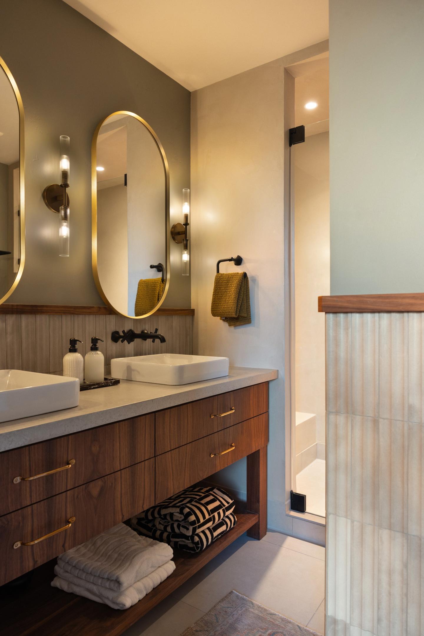 Elegant bathroom with dual mirrors and sinks, wooden vanity, towels below.