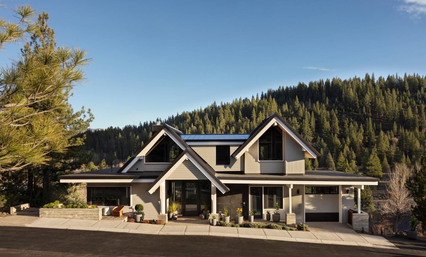 Modern house with large windows, surrounded by tall trees under a clear blue sky.