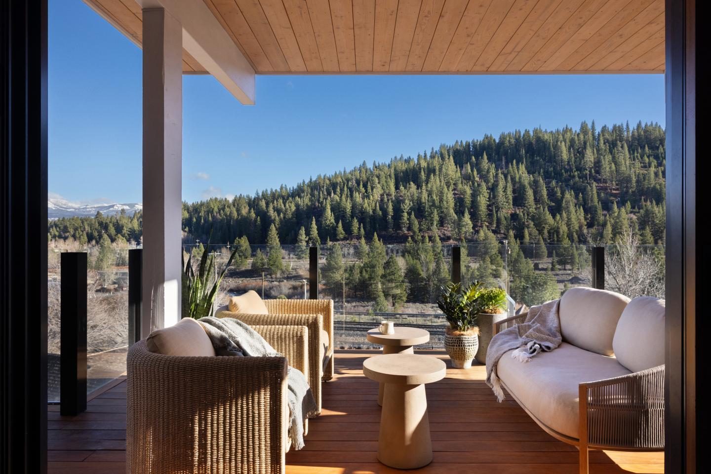 Covered patio with seating overlooking forested hills under a clear blue sky.