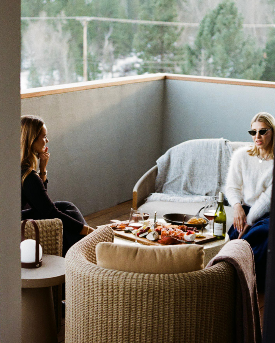 Two people relaxing on a balcony with food and wine.