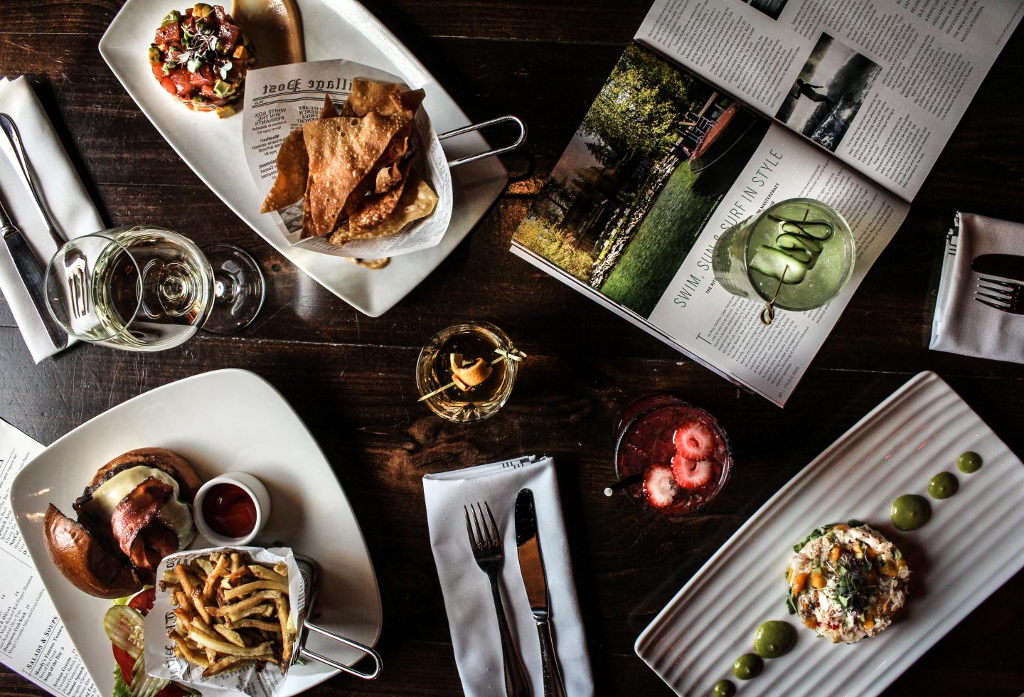 A table with plated food, drinks, and open magazines.