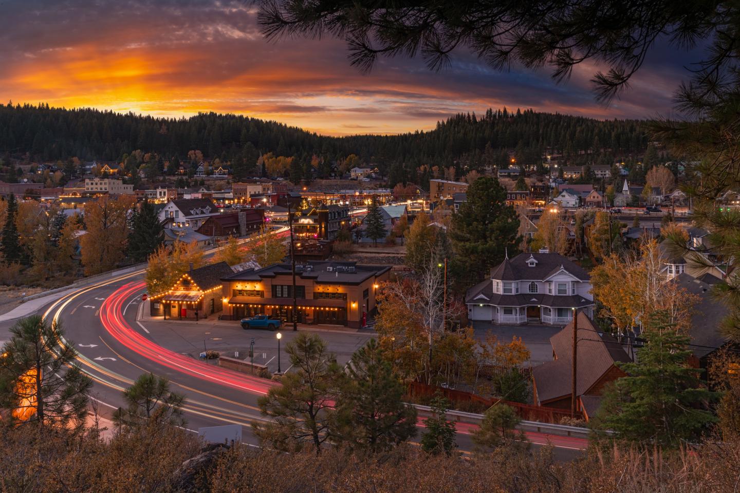 Small town at sunset with vibrant sky and light trails on roads.