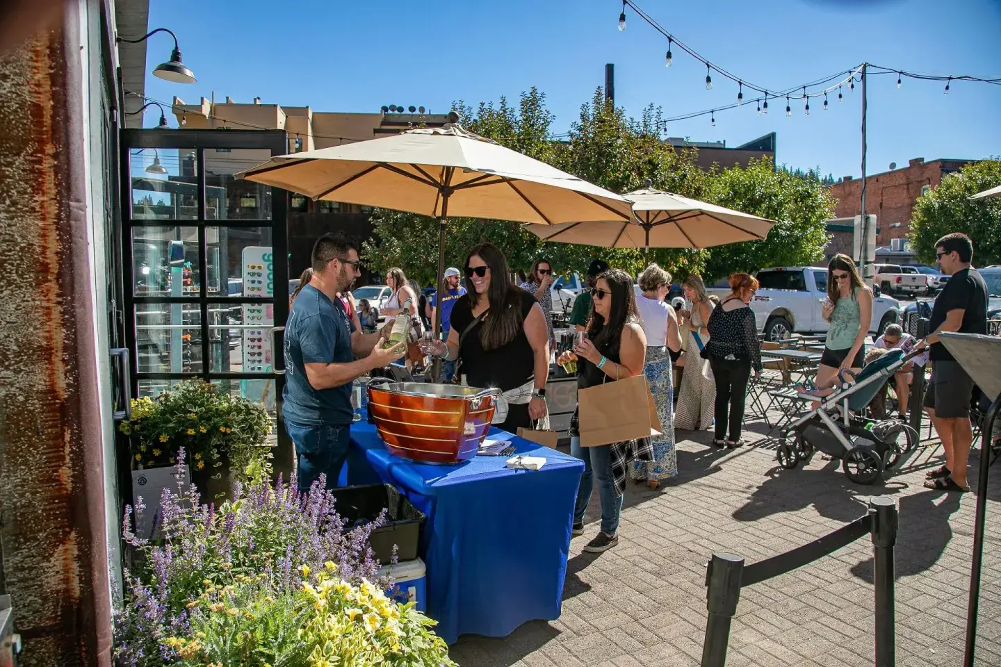 People browse a sunny outdoor market with tables, bicycles, and café umbrellas.