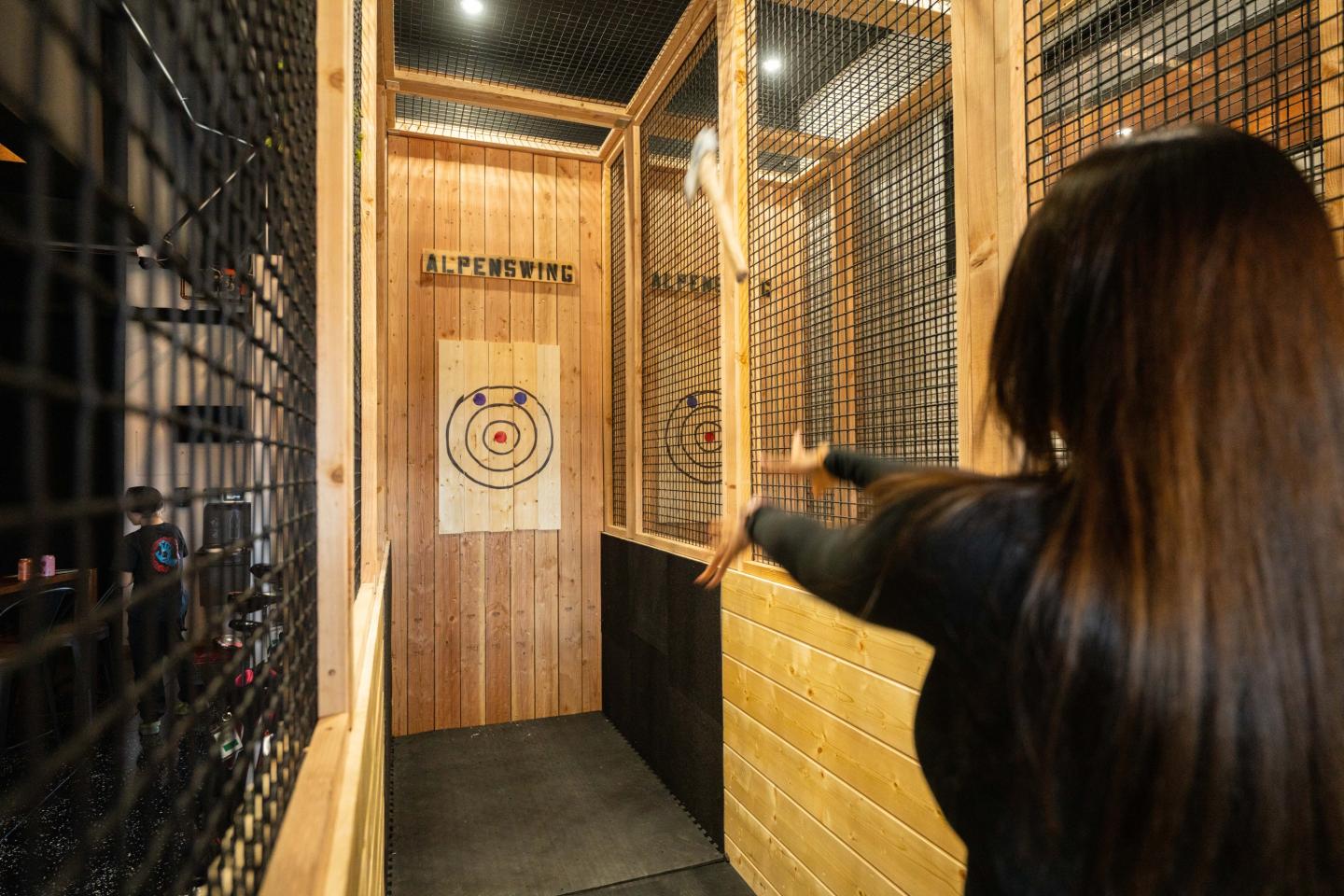 Woman throwing an axe in an indoor axe-throwing lane.