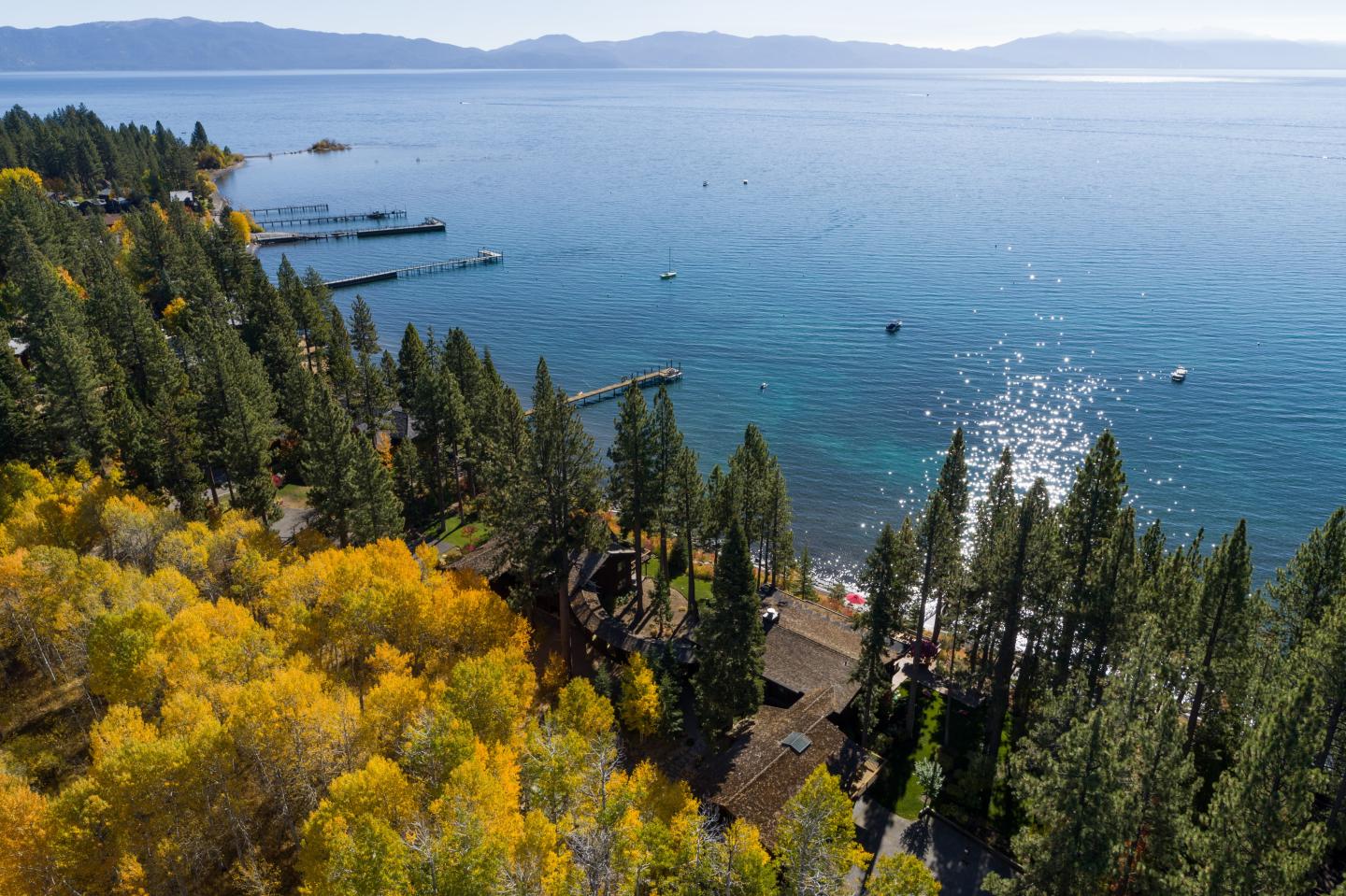 Autumn trees and evergreens overlooking a sparkling blue lake and distant mountains.