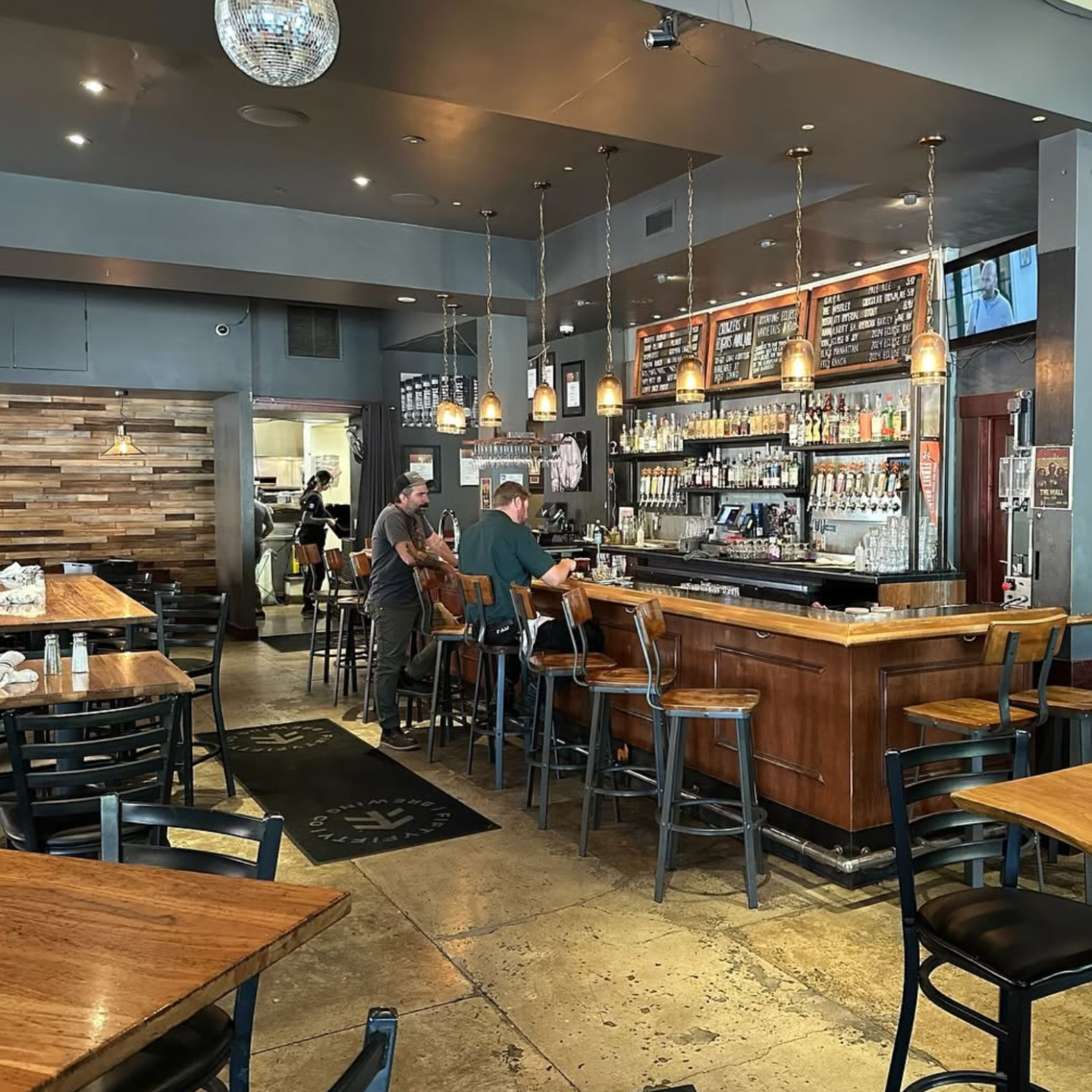 Cozy industrial café bar with wooden tables, pendant lights, and seated patrons.