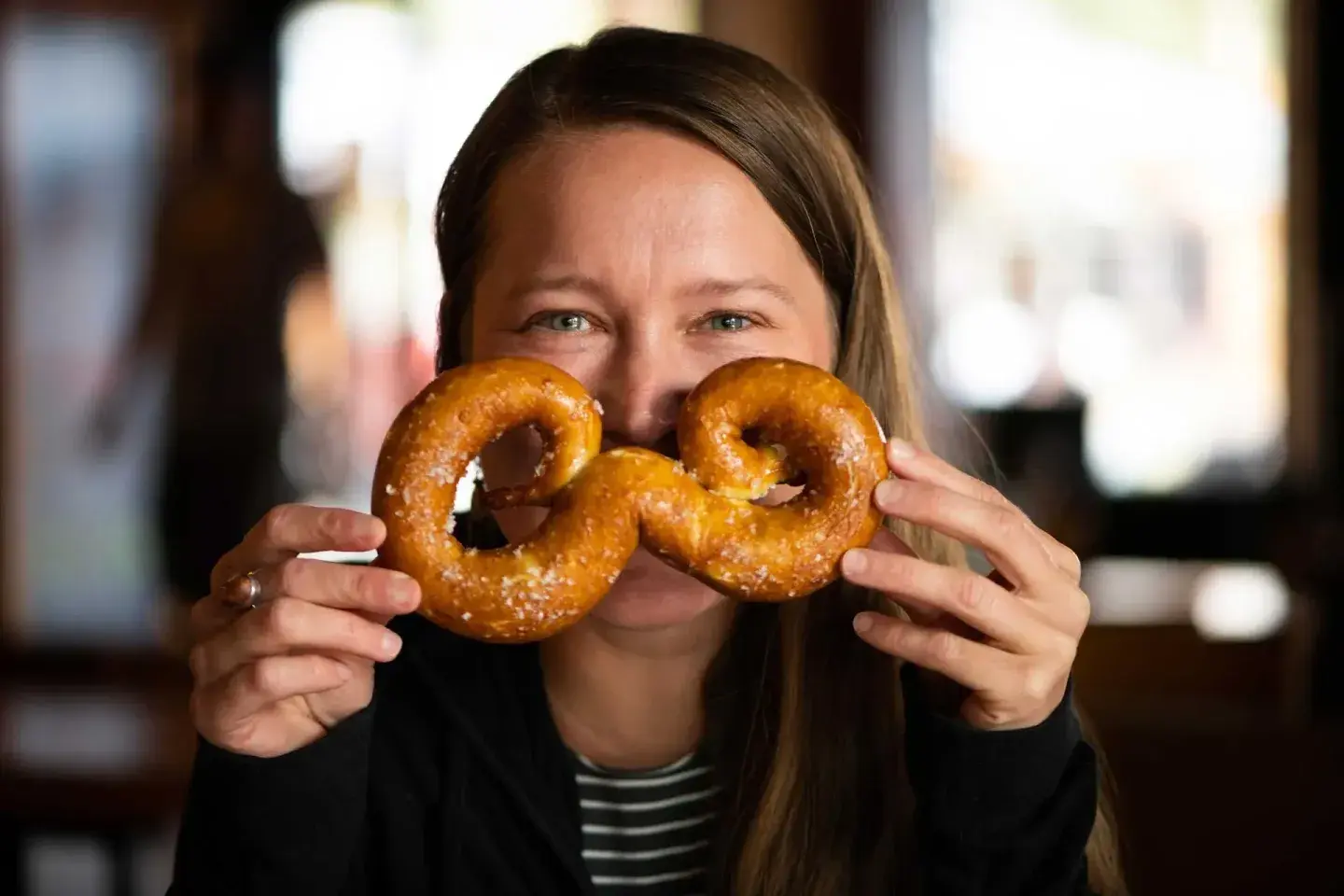 Woman holding two pretzels over her eyes in a café.