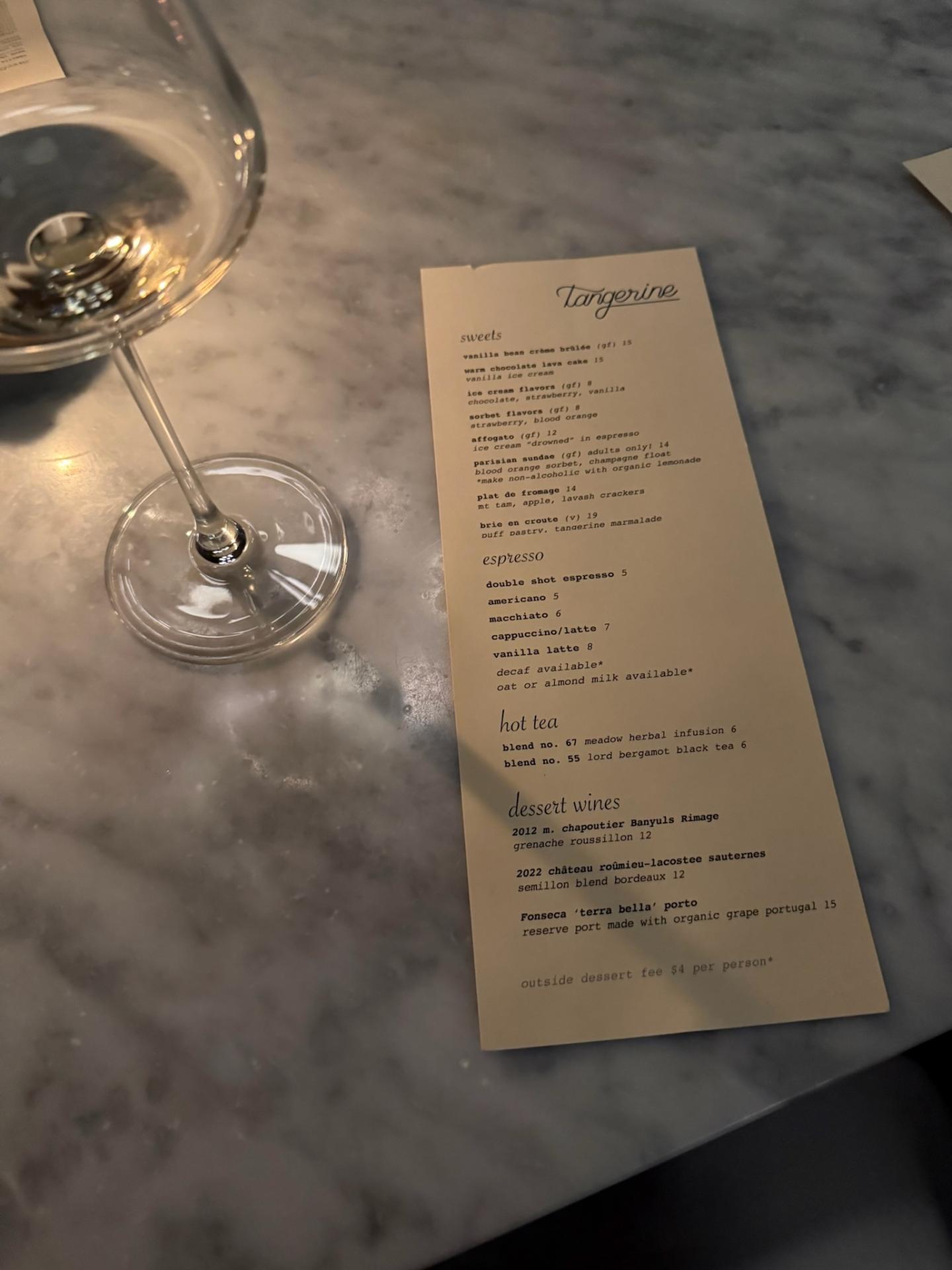 A printed cocktail menu on a marble table beside an empty wine glass.